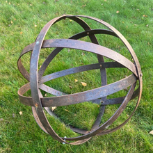 Load image into Gallery viewer, The 80cm Rustic garden ball sculpture on the grass. The rustic garden ball is showing the bolts which hold the bands together.