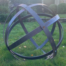 Load image into Gallery viewer, The 80cm Rustic Garden Ball Sculpture sat in the garden with some hedges and small brick wall in the background.