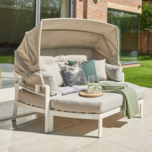 Load image into Gallery viewer, The Titchwell day bed in the garden with the canopy up. There are scatter cushions, a book and tray with drinks on it. 
