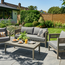 Load image into Gallery viewer, The Arden Rope lounge set in the garden. There are two single chairs and a sofa. The table has a drink some snacks and a plant on it. 
