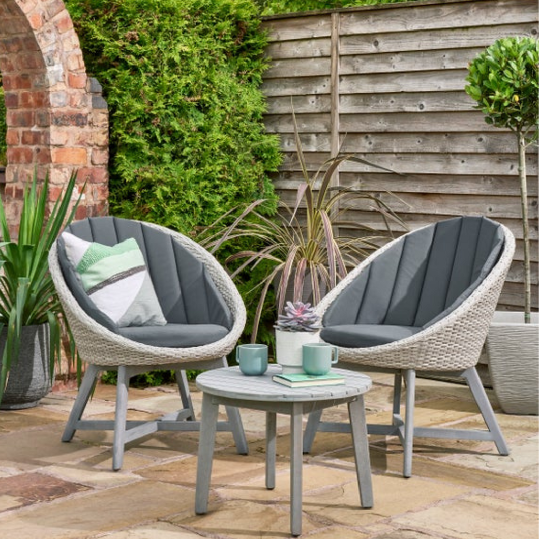 The Chedworth curved bistro set outside on the garden patio with cups and accessories on the table. 