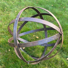 Load image into Gallery viewer, The 80cm Rustic garden ball sculpture on the grass. The rustic garden ball is showing the bolts which hold the bands together.
