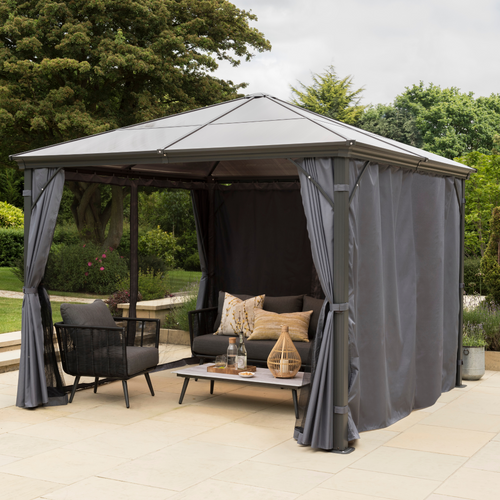 The Runcton Polycarbonate 3m Gazebo with two closed curtains and two open. Shown with garden furniture inside in a garden area. 