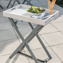Load image into Gallery viewer, The Florenity Grigio Folding Butler Tray outdoors. The table has a bowl of salad on it with some breadsticks in a glass.
