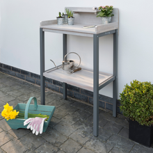 Load image into Gallery viewer, The Florenity Grigio Potting Table with some plants and a watering can on the shelves.
