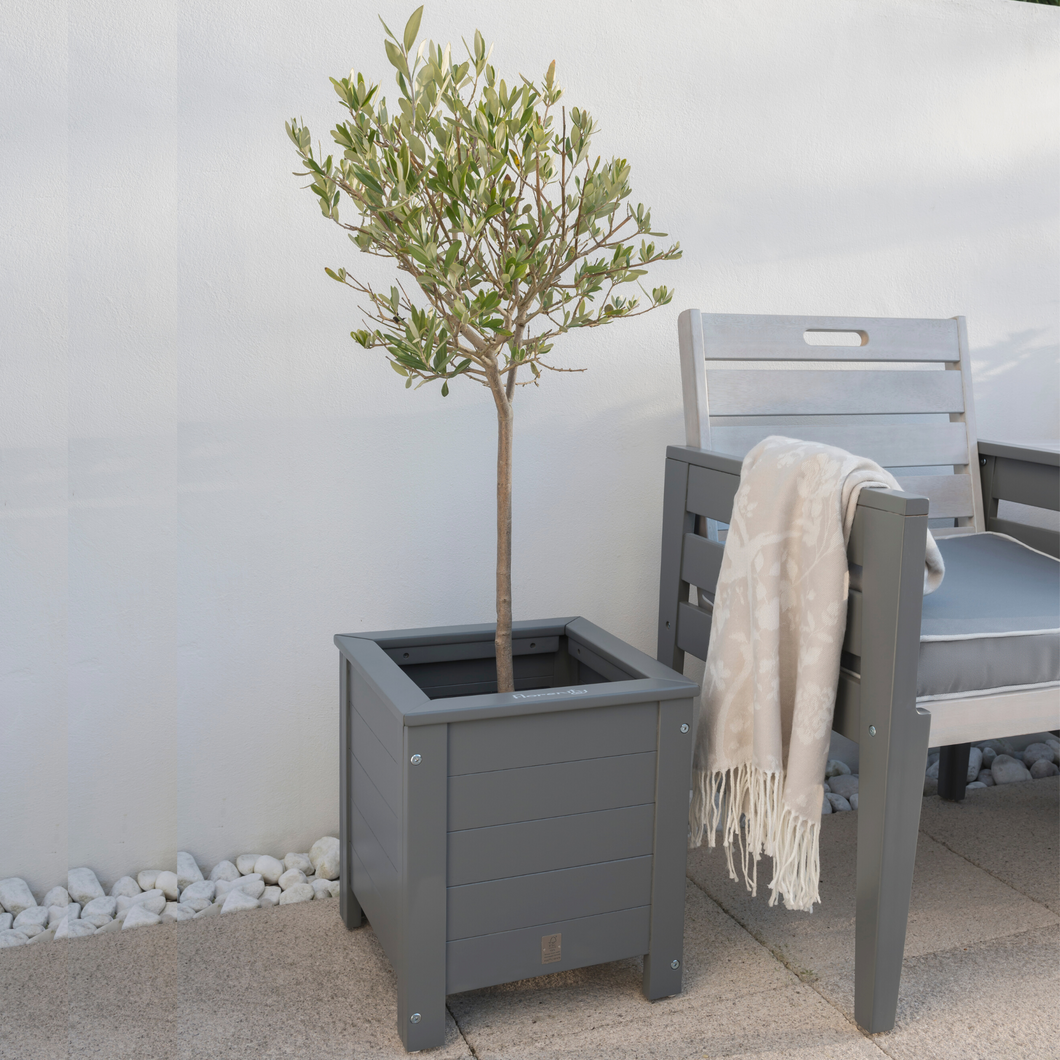 The Florenity Grigio Square Planter outside next to a garden chair with a cream throw over the arm. 