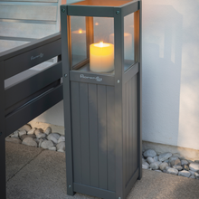 Load image into Gallery viewer, The Florenity Grigio candle lamp outside with a candle burning.
