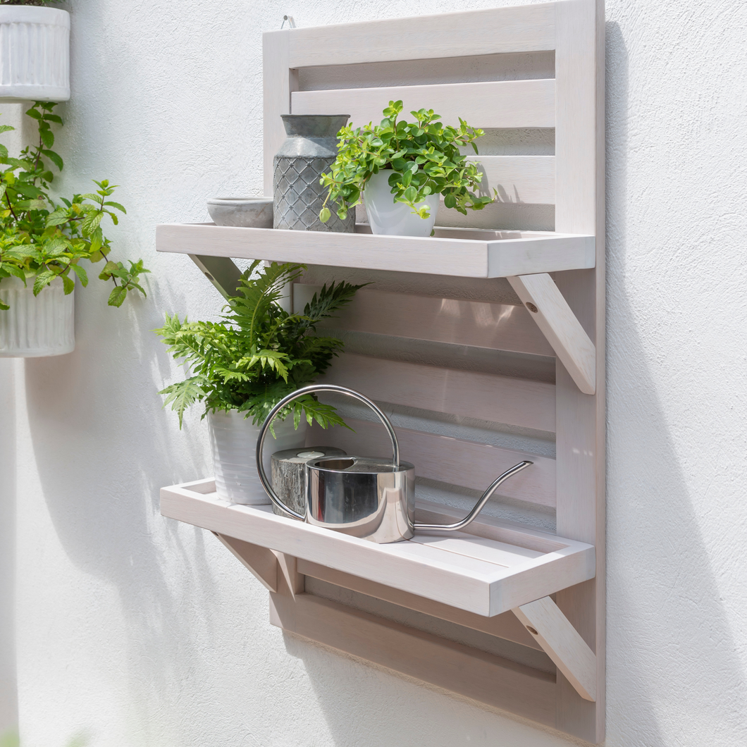 Florenity Galaxy hanging shelf hung on a white garden wall. The shelf has some plants and accessories on. 
