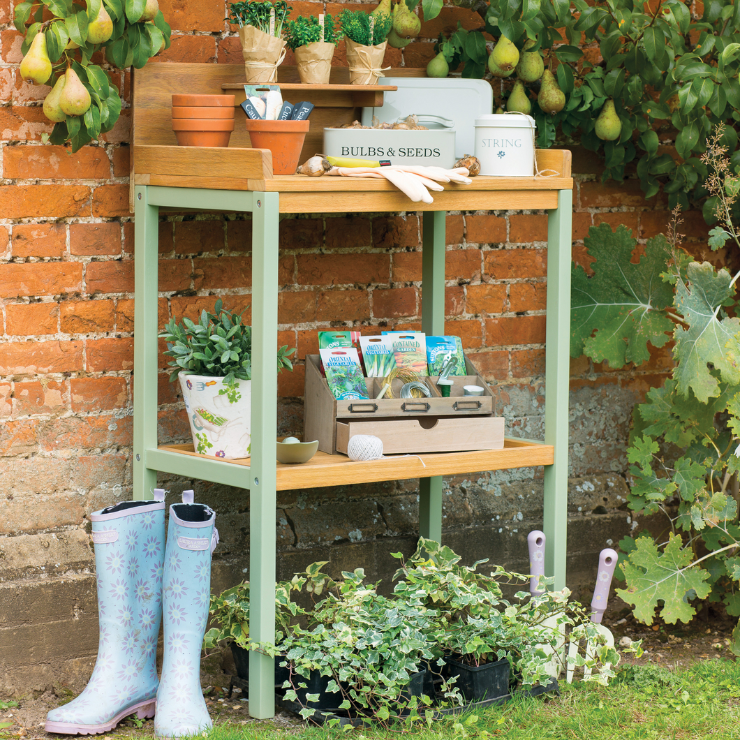 The Florenity Verdi Potting Table outside against a brick wall. The potting bench has pots, gloves and wellies at the side of it. 