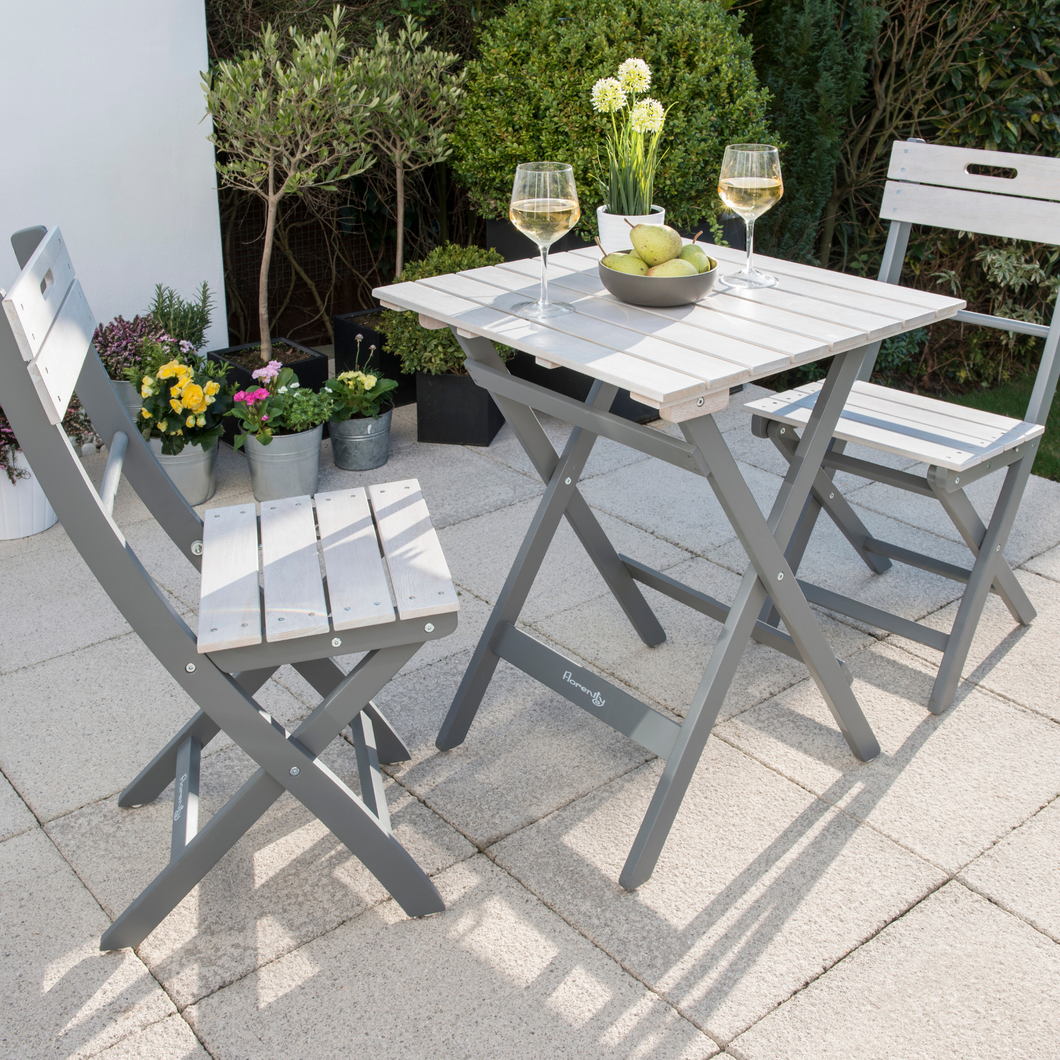 The Florenity Grigio Bistro Set in the garden. There are two glasses of wine and a bowl with pears inside on the table. 