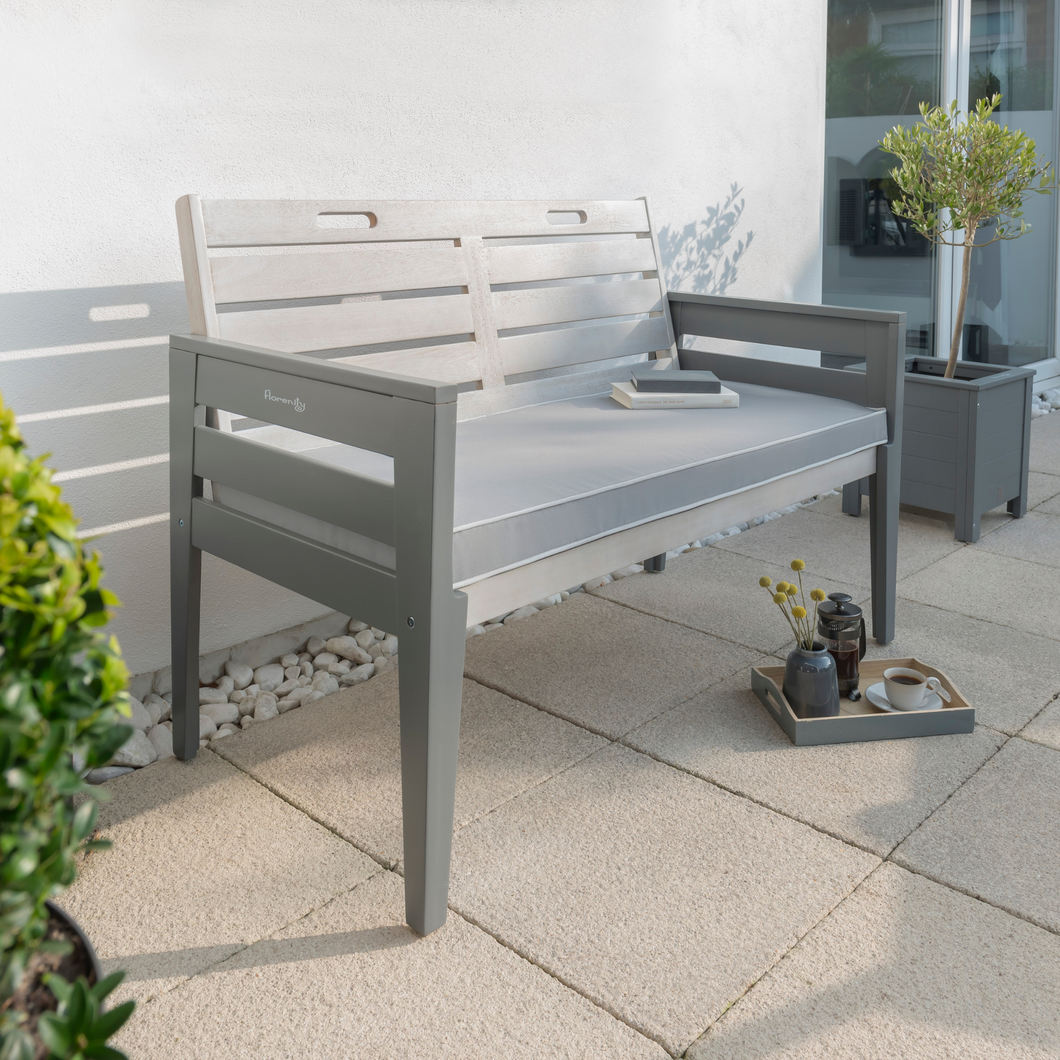 The Florenity Grigio Two Seat Bench Set outdoors against a white wall and plants either side. There is a tray below the bench with a cup of coffee and a plant on. 