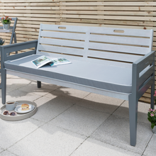 Load image into Gallery viewer, The Florenity Grigio three seat bench set in a grey finish. The bench has a newspaper open on it and a tray with a bun and coffee on underneath. 
