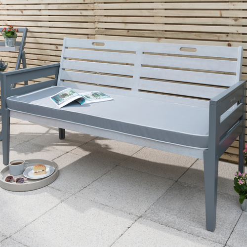 The Florenity Grigio three seat bench set in a grey finish. The bench has a newspaper open on it and a tray with a bun and coffee on underneath. 