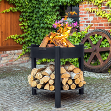 Load image into Gallery viewer, The Cook King Montana 80cm Fire Pit High with fire lit outside. The storage shelf underneath also has wood stored on it. 
